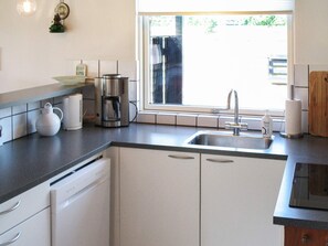 A kitchen with a dishwasher, coffee maker, kettle, and a window with a view of greenery. - 5 Person Holiday Home in Vaeggerlose (Vaeggerlose)