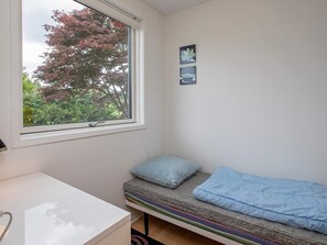 Una habitación pequeña con cama individual, ventana, mesita de noche y dos cuadros colgados en la pared.