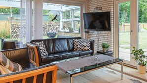 Een moderne woonkamer met een leren bank, een glazen salontafel en een flatscreen televisie die aan een bakstenen muur is bevestigd.
