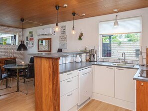 A modern kitchen with a central island, white cabinetry, and a window providing natural light. - 5 Person Holiday Home in Vaeggerlose (Vaeggerlose)