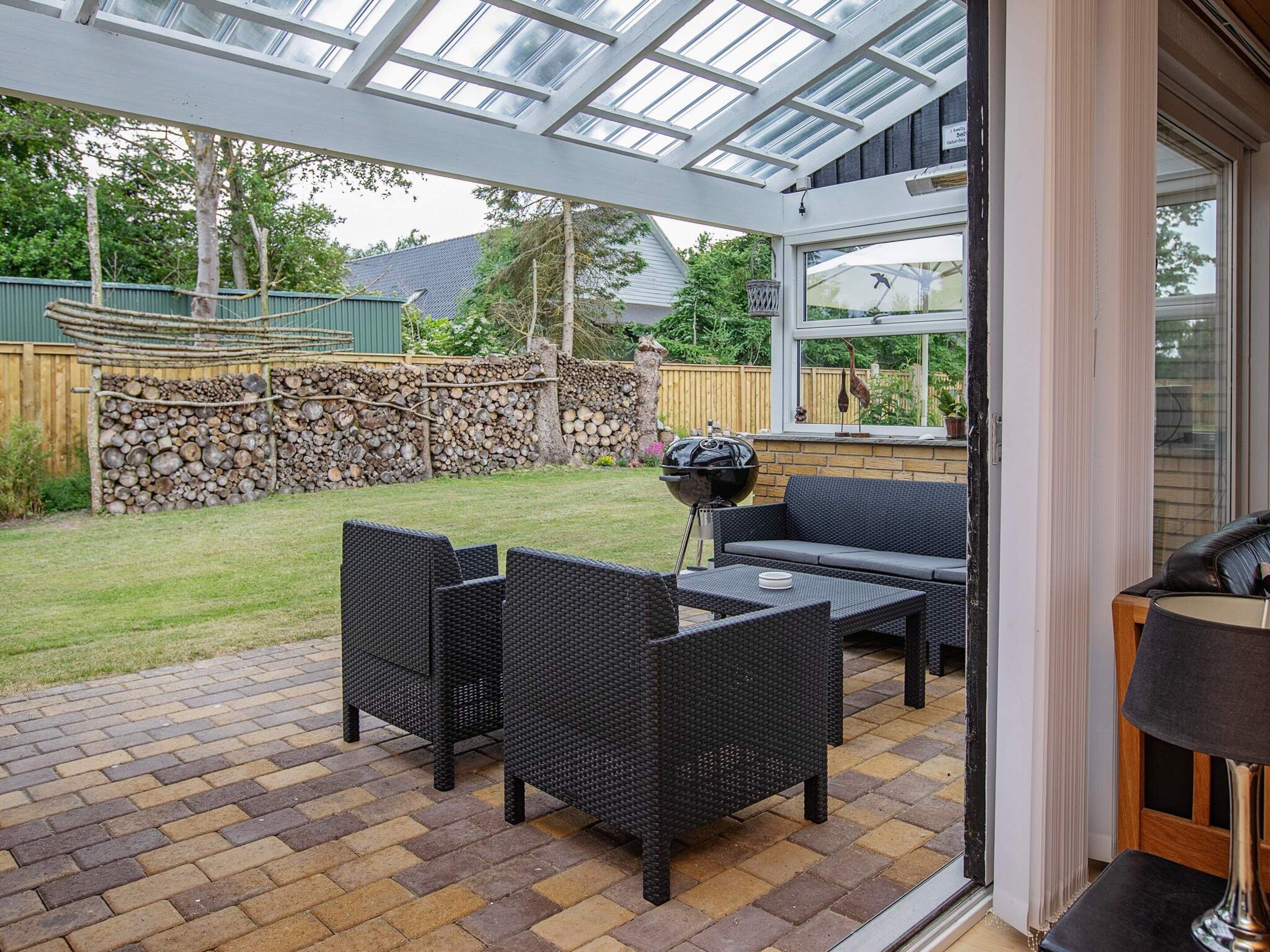 An outdoor patio with wicker furniture, a grill, and a stone wall.