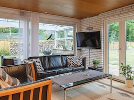 A modern living room with a leather sofa, a glass coffee table, and a flat-screen TV mounted on a brick wall.