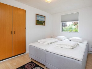 A bedroom with a double bed, a wardrobe, a window with a view of greenery, and a painting on the wall.