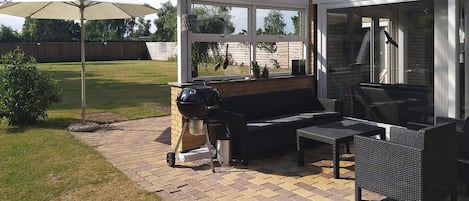 An outdoor patio with a grill, seating, and a covered area with a view of the backyard.