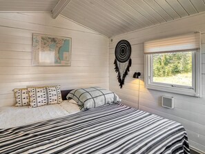 A bedroom with a bed, a map on the wall, a dreamcatcher, and a window with a view of trees.