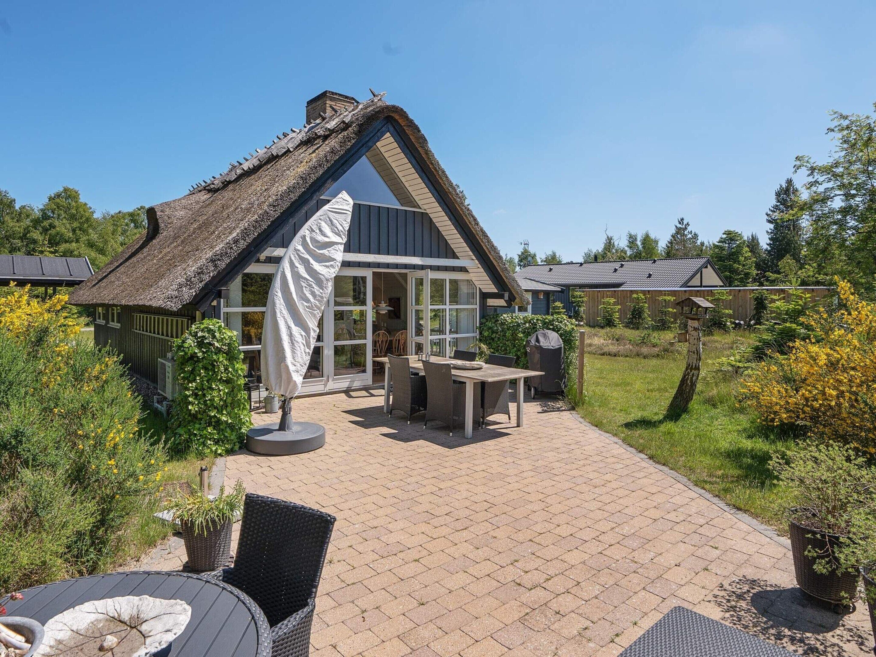 A thatched-roof house with a patio area featuring outdoor furniture and a fire pit.