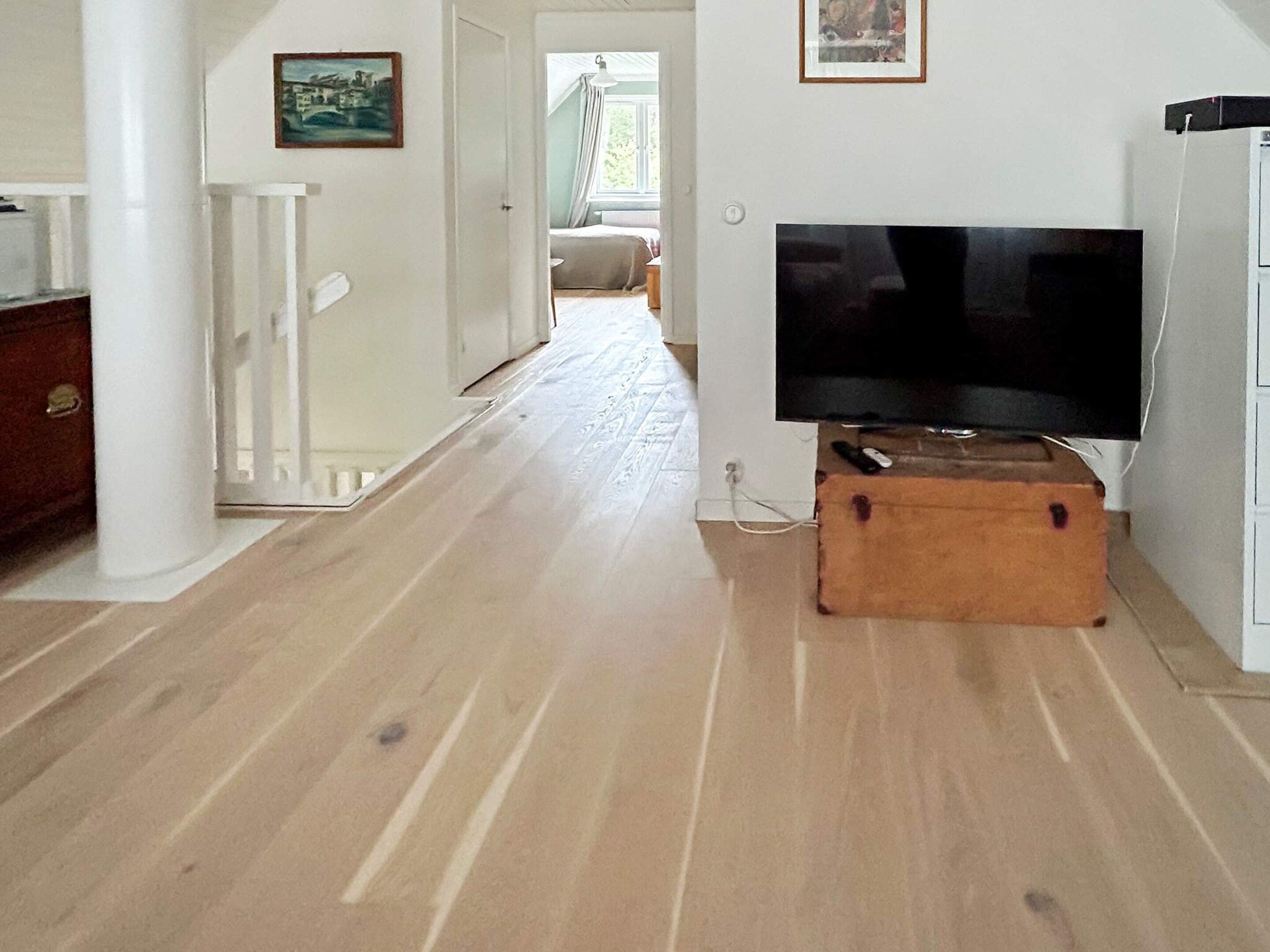 A hallway with a wooden floor, a television on a stand, and a door leading to another room.