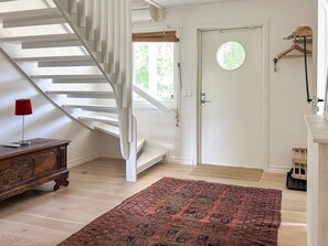 A staircase leading to a door with a window, a red lamp, a wooden dresser, and a patterned rug.