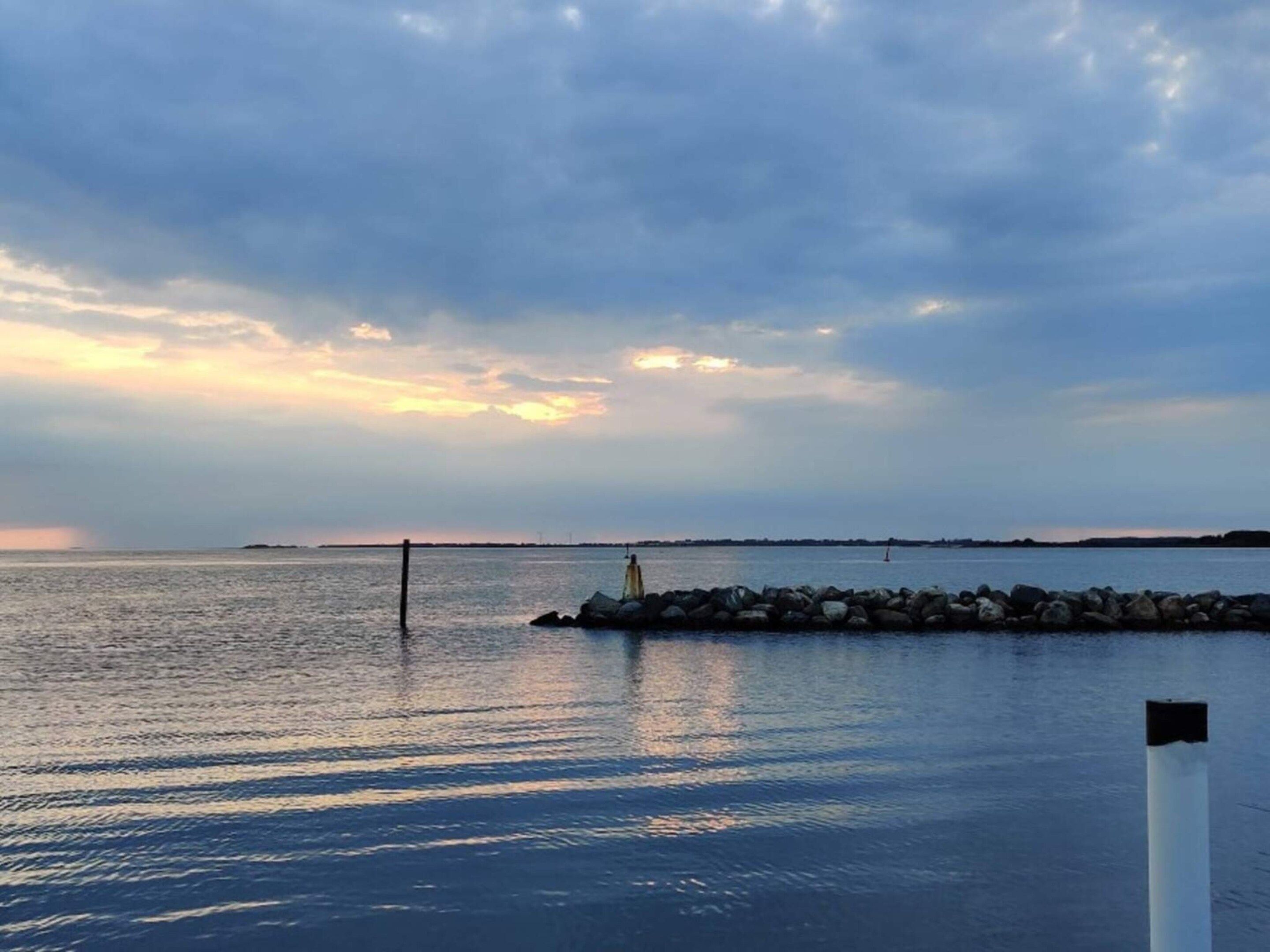 A calm body of water with a rocky breakwater and a distant shoreline.