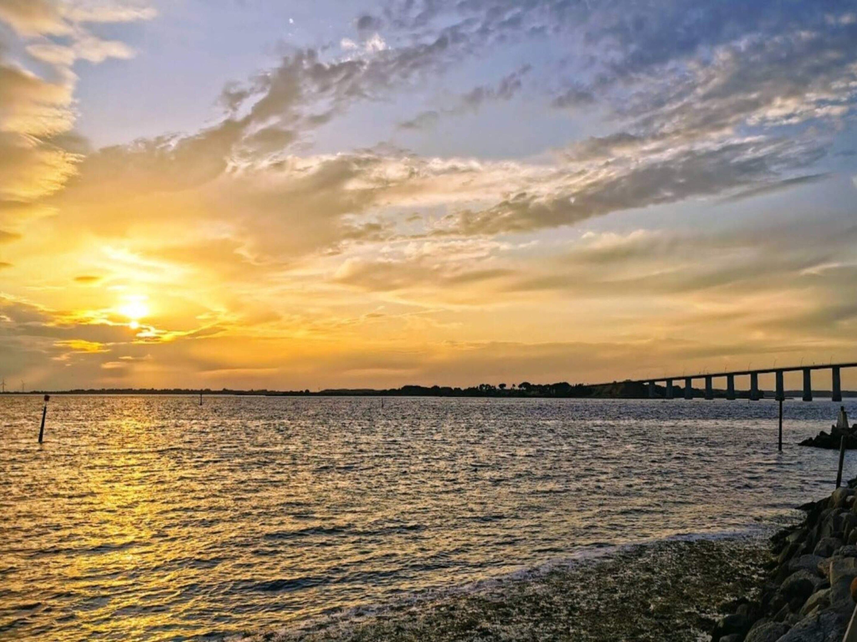 Un atardecer sobre una masa de agua con un puente a lo lejos.