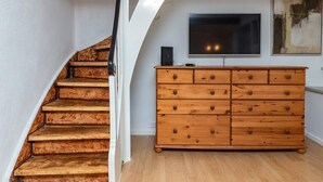Een trap met houten treden en een witte muur, een houten dressoir met laden, en een flatscreen televisie aan de wand bevestigd.