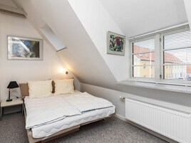 Un dormitorio con cama, mesita de noche, lámpara, radiador y dos cuadros en la pared.