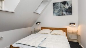 Een slaapkamer met een schuine plafond, een bed met witte beddengoed, twee bedlampen en een schilderij aan de muur.