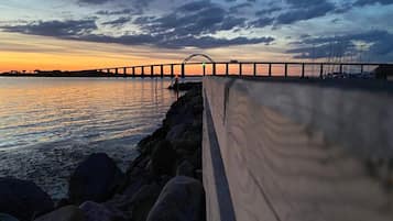 A sunset view of a bridge over water with a wooden walkway along the shore.