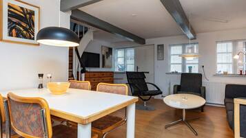 Ein modernes Wohnzimmer mit Essbereich, ausgestattet mit einem weißen Tisch, Holzstühlen, einem schwarzen Ledersessel und einem weißen Couchtisch.