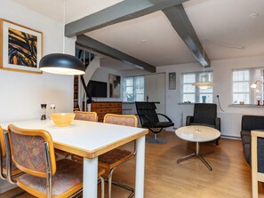 A modern living room with a dining area, featuring a white table, wooden chairs, and a black sofa. - 4 Person Holiday Home in Rudkobing (Rudkobing)