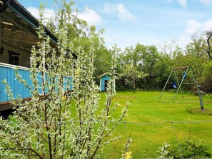A backyard with a blue shed, a swing set, and a tree in front of a house. - 7 Person Holiday Home in Hova (Hova)