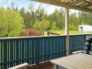A covered outdoor area with a wooden deck, a metal railing, and a view of a forested area with a birdhouse. - 7 Person Holiday Home in Hova (Hova)