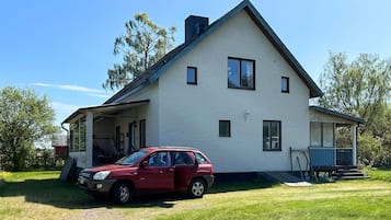 A two-story house with a covered porch and a red car parked in front.