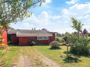 A red house with a tiled roof, a small garden with a pathway leading to the entrance, and a clear blue sky. - 5 Person Holiday Home in Bogo By (Bogø By)