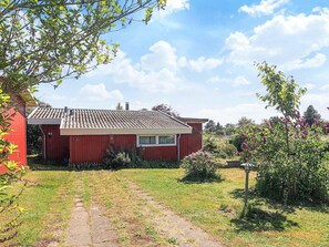 A red house with a tiled roof, a paved driveway, and a garden with various plants and flowers. - 5 Person Holiday Home in Bogo By (Bogø By)