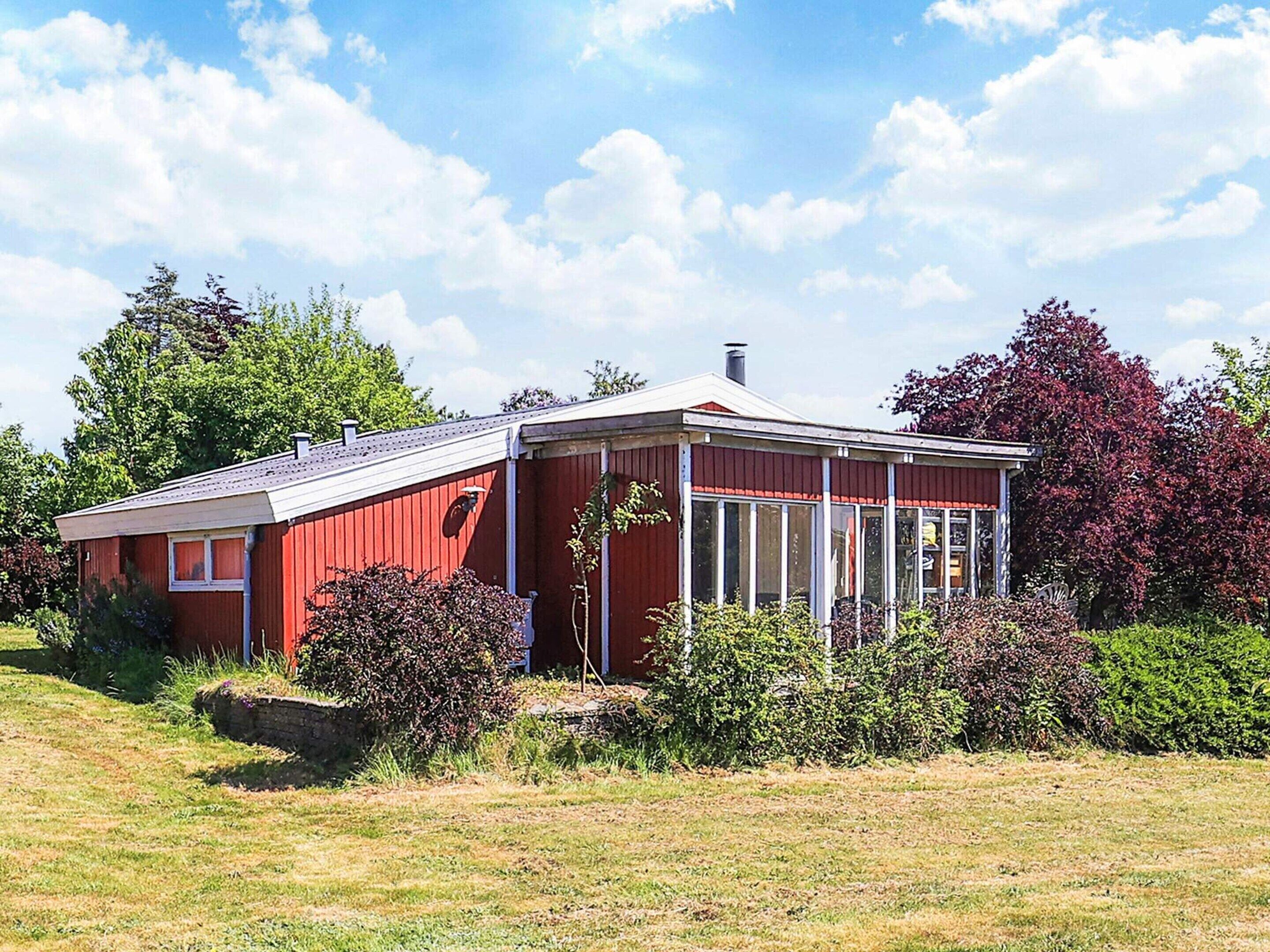 A red wooden house with a sloped roof and a covered porch.