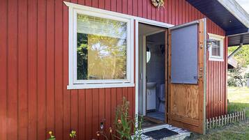 A red wooden building with a door leading to a bathroom, a window, and a small porch area.