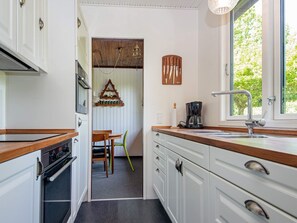 A kitchen with white cabinets, a wooden countertop, a coffee maker, and a window with a view of greenery. - 4 Person Holiday Home in Ans By (Ans)