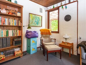 Un rincón acogedor para leer, con una estantería, una silla, una mesita y una ventana con vistas a la vegetación.