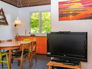 A room with a wooden dining table, chairs, a flat-screen TV on a wooden stand, a window with a view of greenery, and a painting on the wall. - 4 Person Holiday Home in Ans By (Ans)