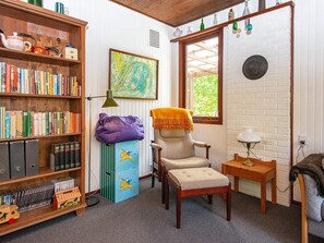 Un rincón acogedor para leer, con una estantería, un sillón, una mesita y una ventana con vistas al verdor.
