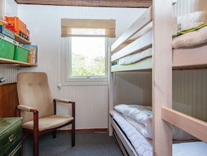 Una habitación pequeña con literas, una silla, una ventana y estantes llenos de juguetes y libros.