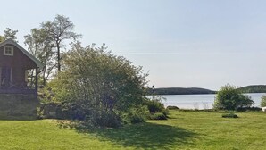 A grassy area with a wooden cabin and a view of a lake. - 6 Person Holiday Home in Boxholm-by Traum (Boxholm)