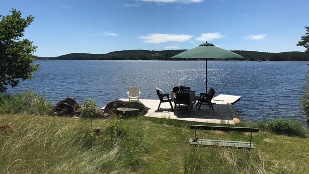 A lakeside patio with outdoor seating and a green umbrella. - 6 Person Holiday Home in Boxholm-by Traum (Boxholm)