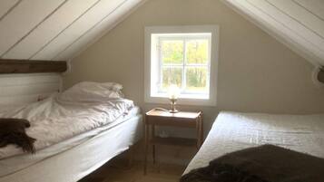 A small attic bedroom with two beds, a window, and a nightstand with a lamp.