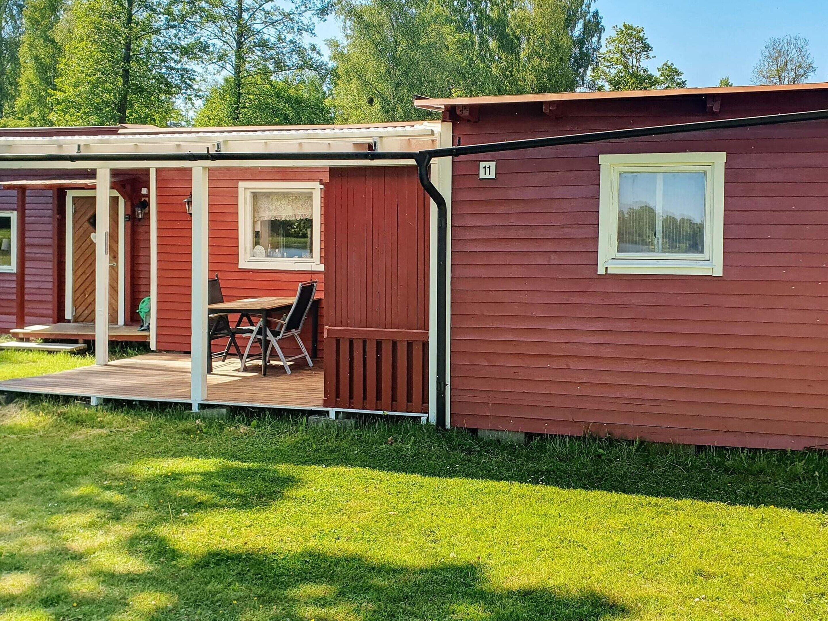 A red cabin with a wooden deck, a table, and chairs outside.