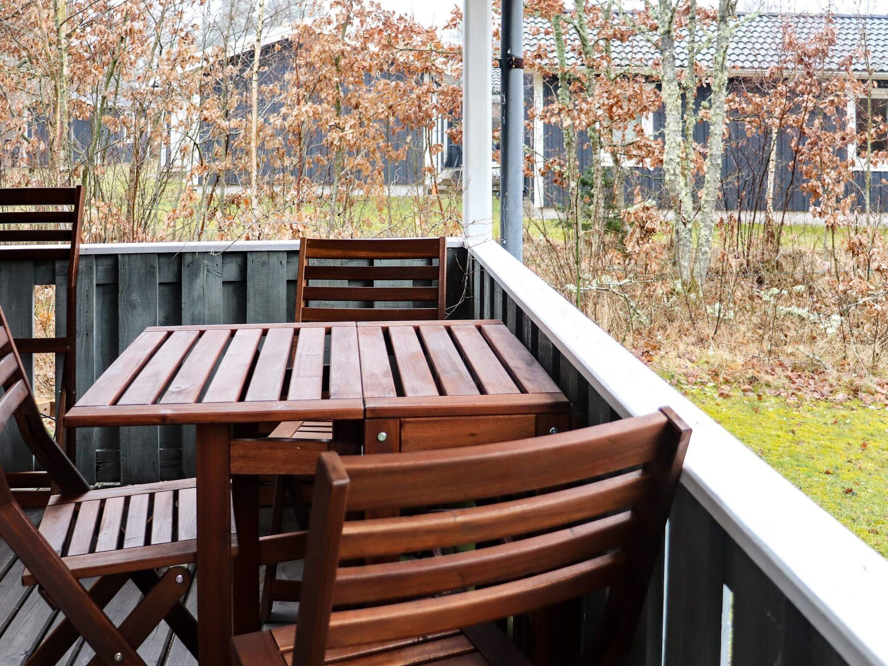 A wooden deck with a table and chairs, surrounded by a wooden fence and trees.