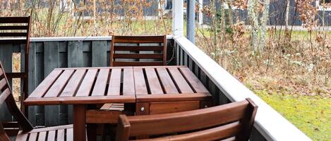 A wooden deck with a table and chairs, surrounded by a wooden fence and trees.
