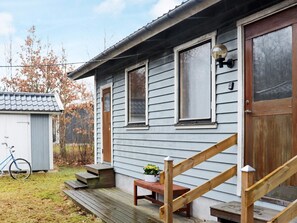 Ett tvåvåningshus med en trätrappa som leder till ytterdörren, en liten veranda med en bänk och en cykel som står parkerad utanför.