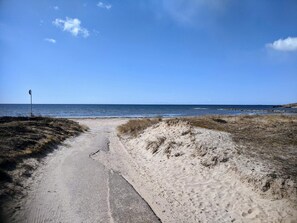 Um caminho de areia serpenteia até o mar sob um céu limpo.