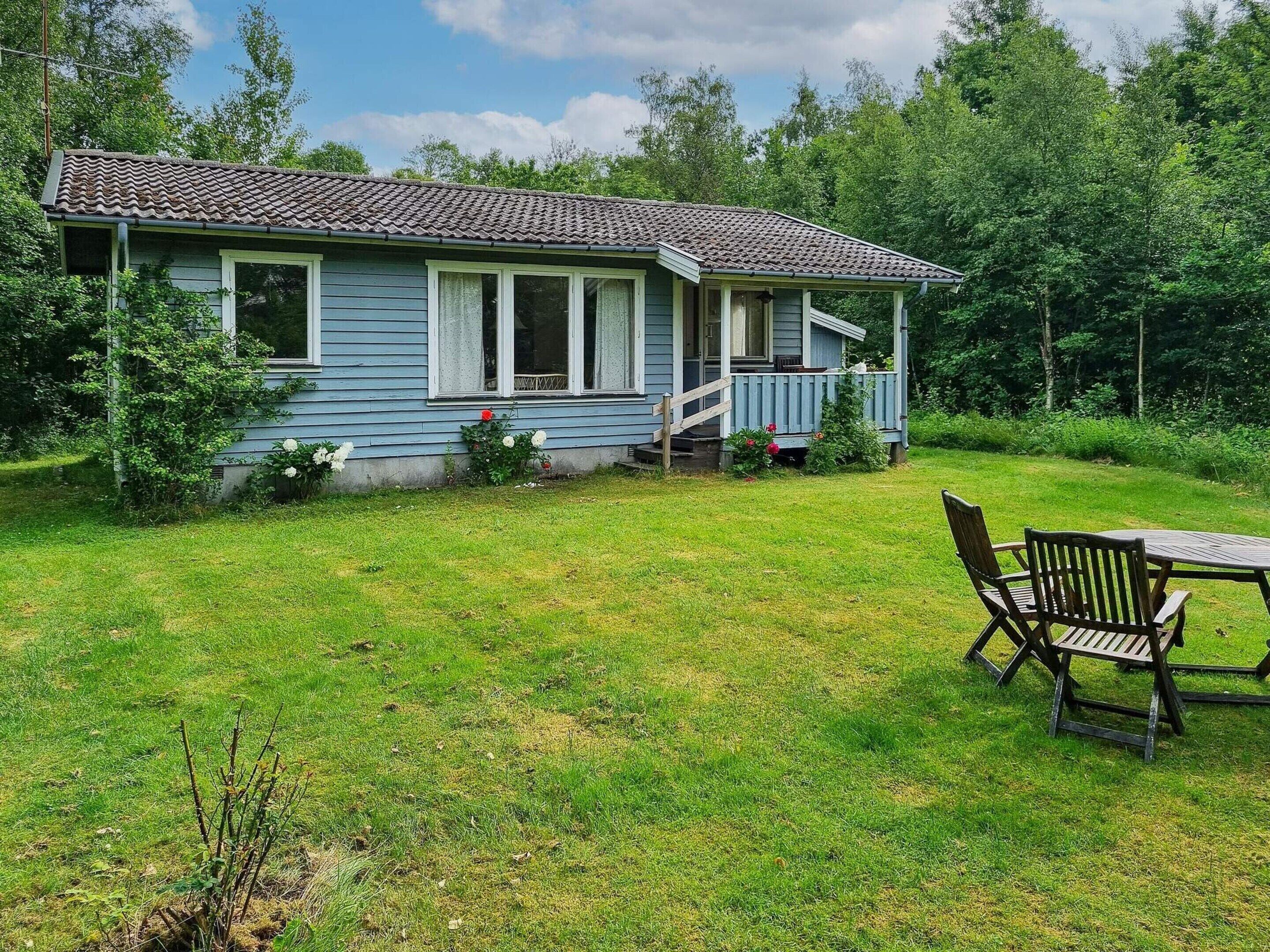 A single-story house with a porch, surrounded by a grassy yard and trees.