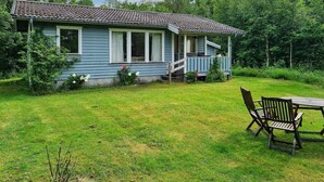 A single-story house with a porch, surrounded by a grassy yard and trees. - 4 Person Holiday Home in Heberg (Heberg)