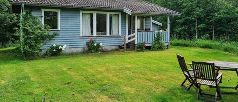 A single-story house with a porch, surrounded by a grassy yard and trees.