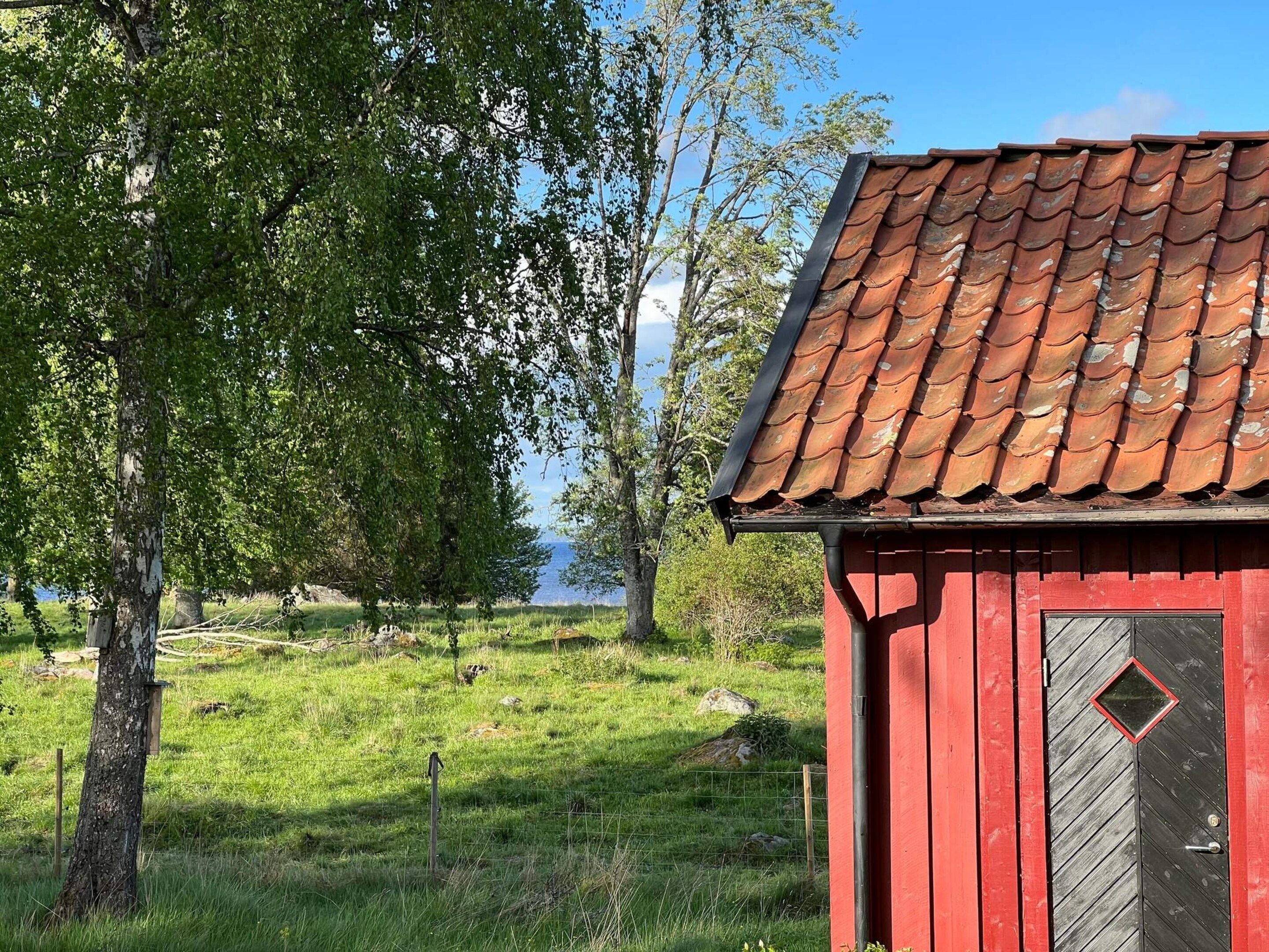 A red wooden building with a tiled roof, surrounded by grass and trees.