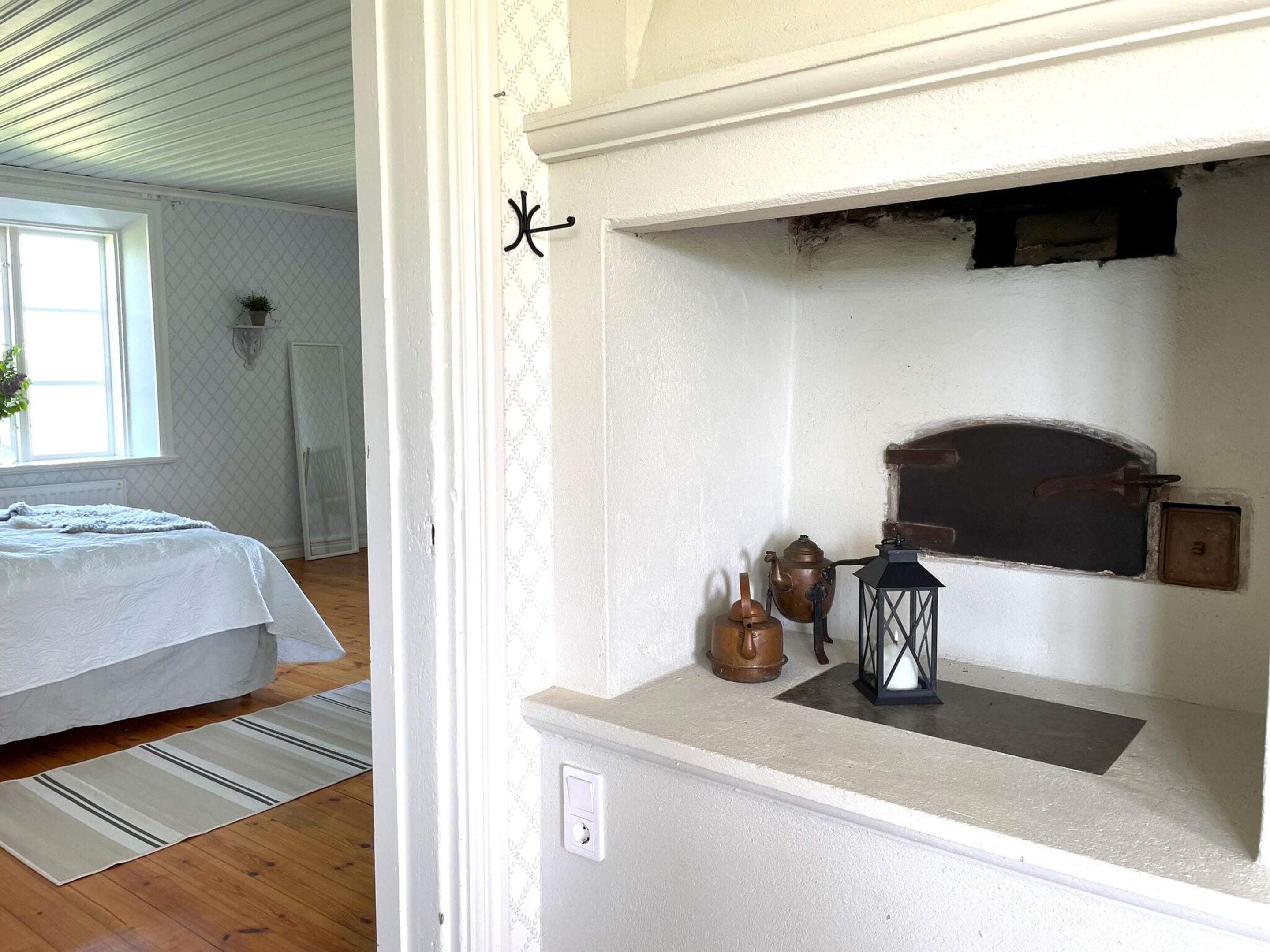 A bedroom with a bed, a window, and a wall-mounted shelf with a lantern and a teapot.