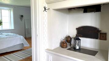 A bedroom with a bed, a window, and a wall-mounted shelf with a lantern and a teapot.