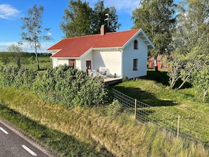 Une maison blanche avec un toit rouge, entourée de verdure et d’une clôture.