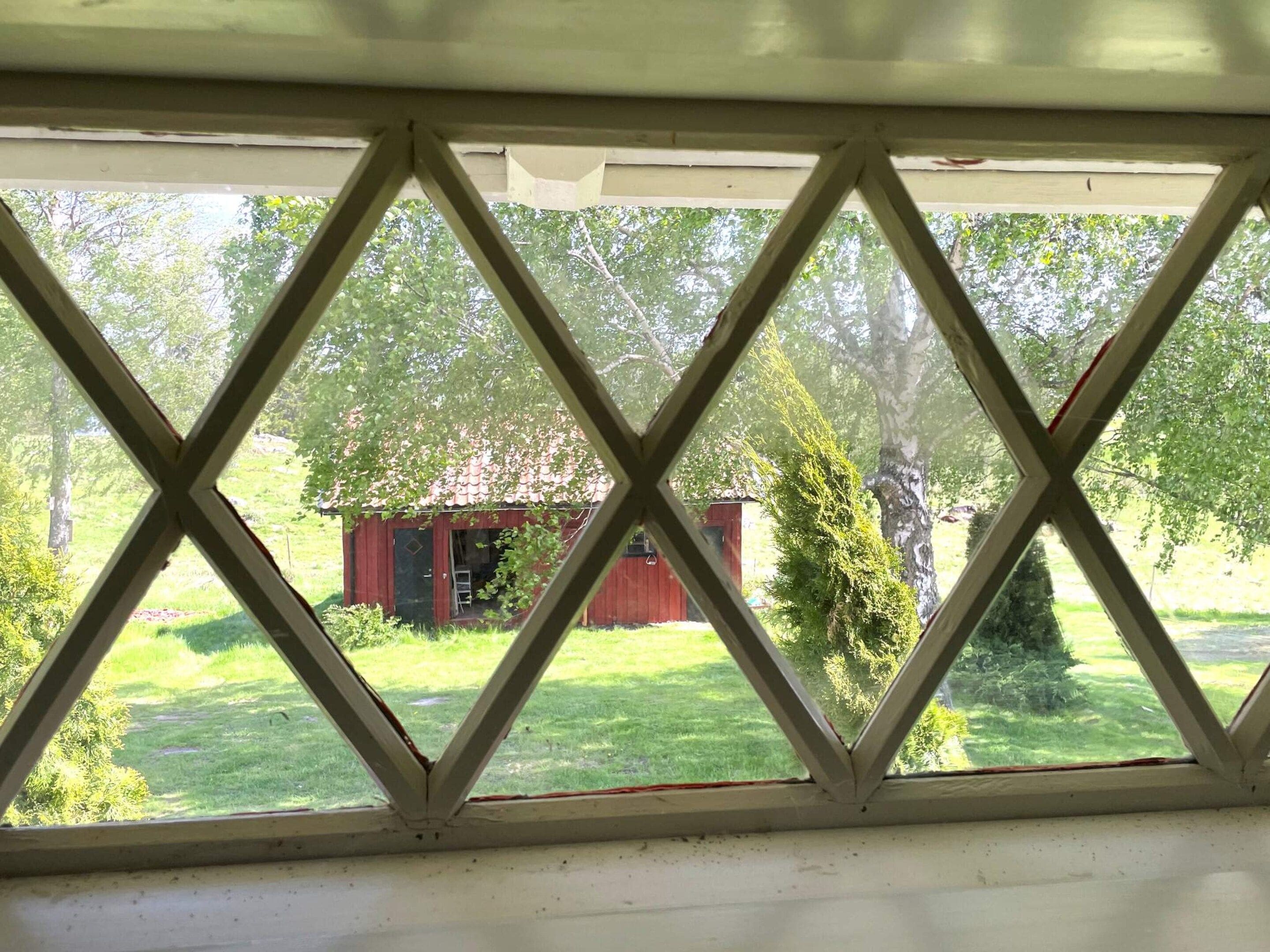 A view through a diamond-patterned window of a red barn and green landscape.