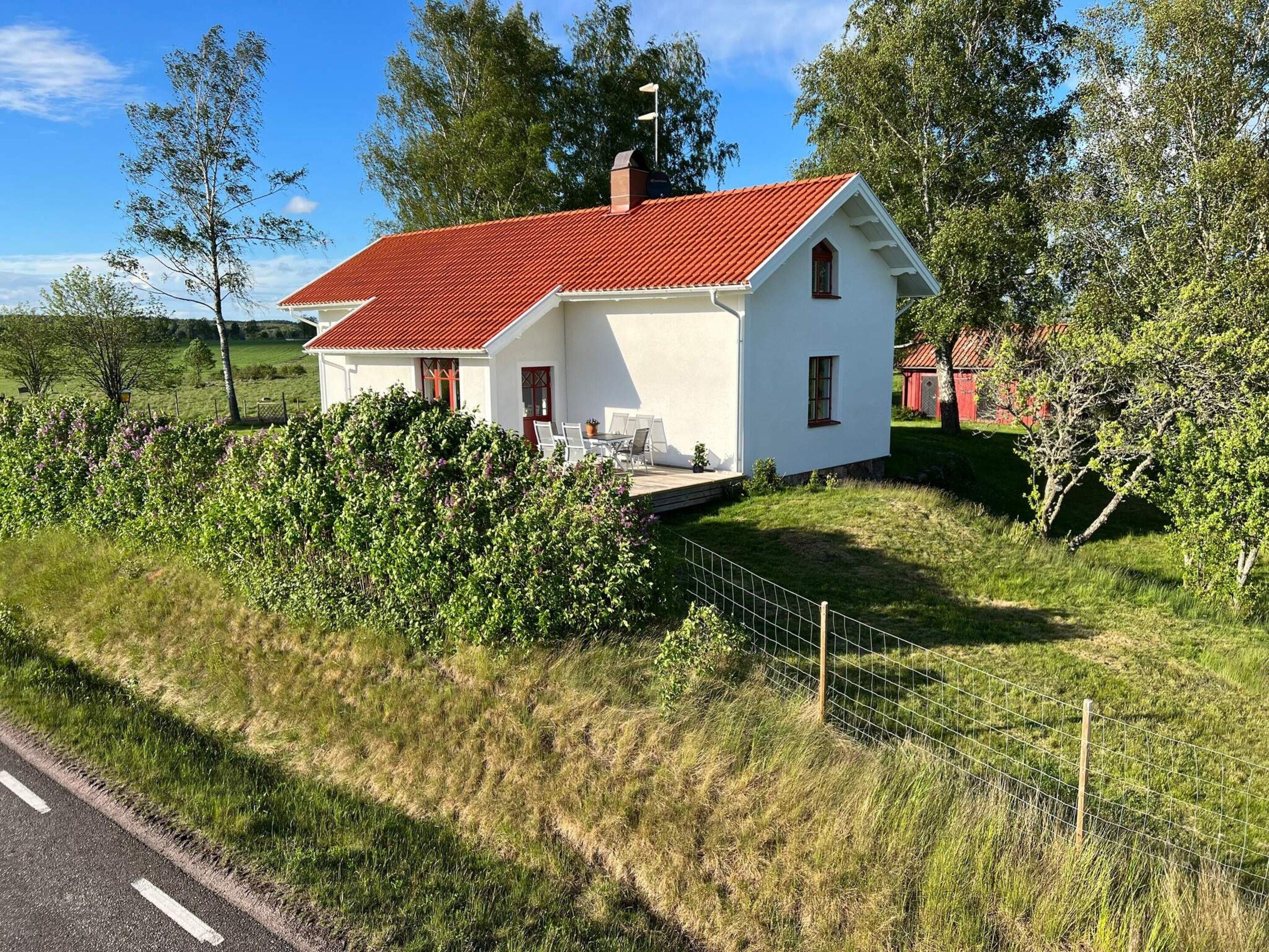 Een wit huis met een rood dak, omgeven door groen en een hek.