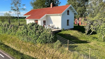 Een wit huis met een rood dak, omgeven door groen en een hek.